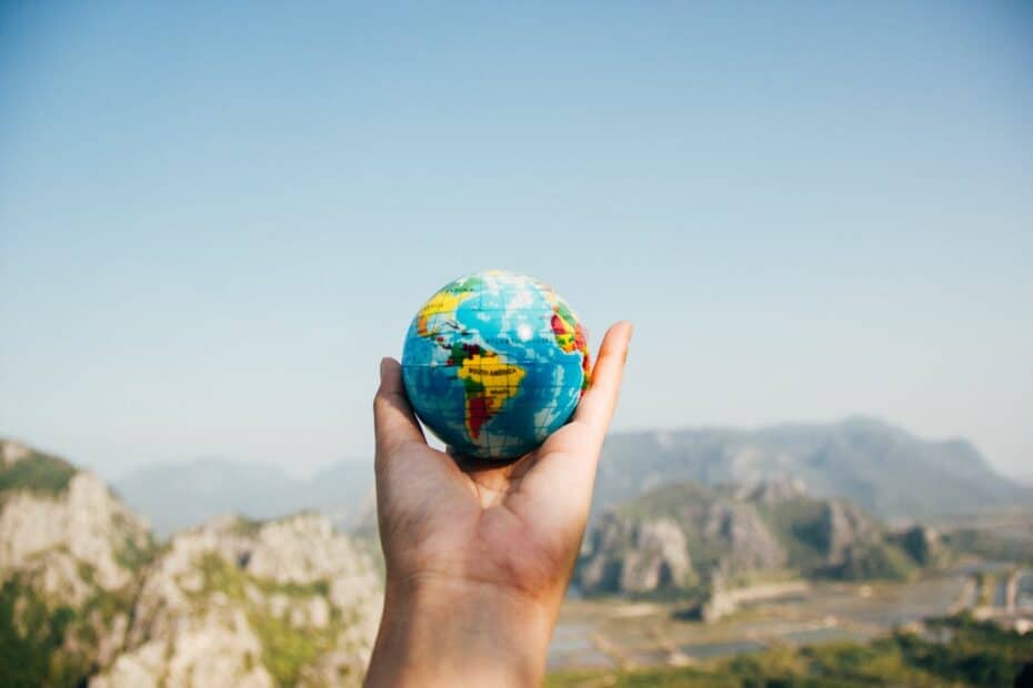 A person holding a globe over a mountain.