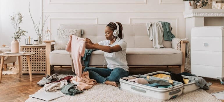 Person packing clothes in a suitcase while listening to music, preparing for a move to a different state.