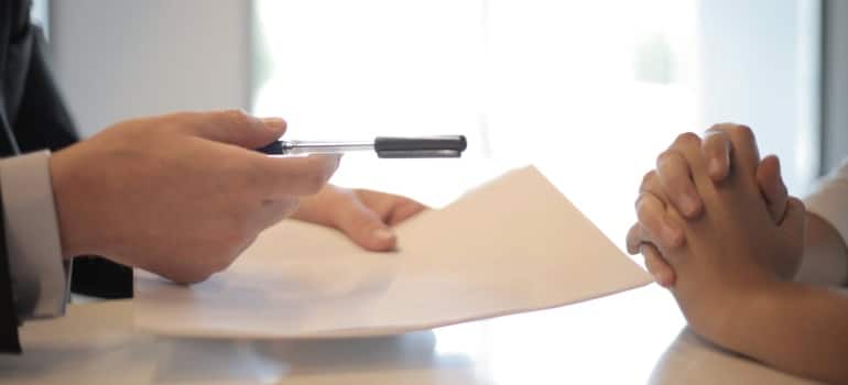 a person handing a pen and paper to another person