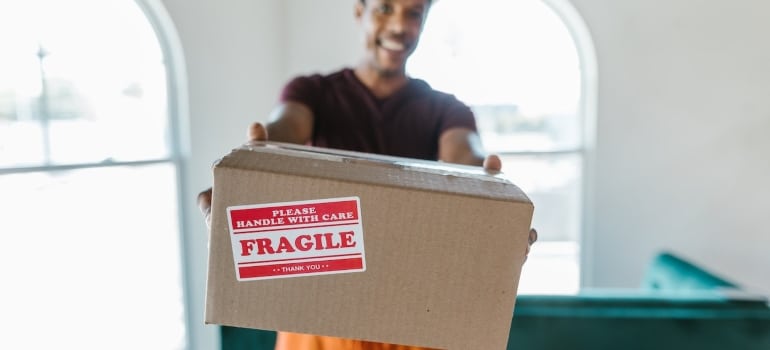 a man smiling and holding a box labeled 'fragile' thinking about storage hacks for home renovation